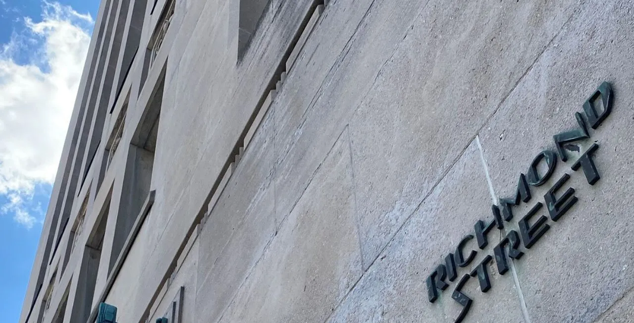 an image of a grey-brick building captured from below. On the building is a sign reading 