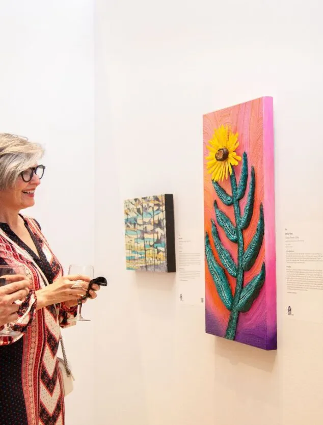 Two people are standing in front of three vibrant works of art, admiring them and conversing.
