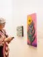 Two people are standing in front of three vibrant works of art, admiring them and conversing.