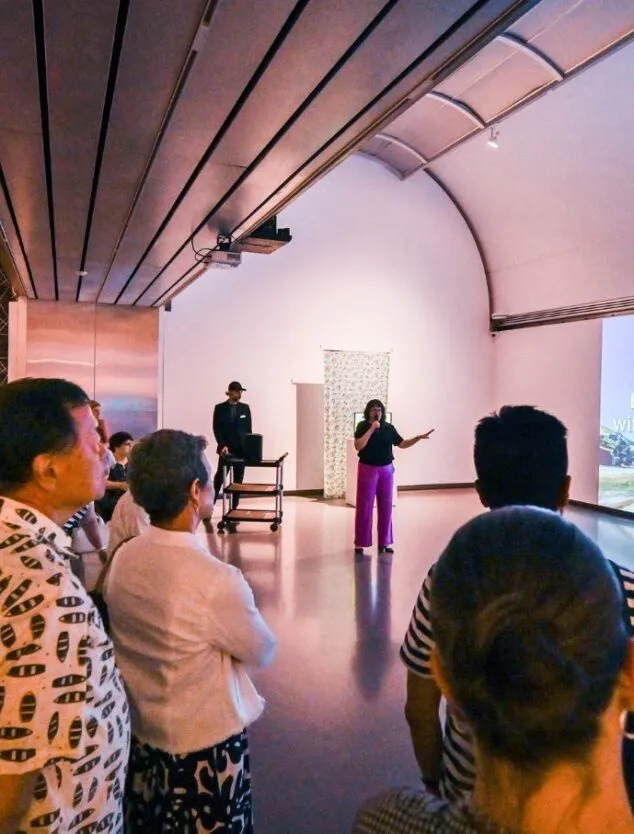 a crowd surrounds a curator in a gallery to learn about the artworks and artifacts on display