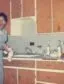 two women in formal attire stand in a 1960s kitchen with wood cupboards and tile backsplash. The woman on the left is looking at the camera.