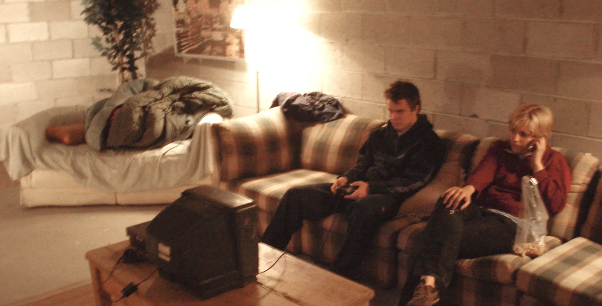a blurry, warm toned image of two individuals seen sititng on a plaid couch and watching a small television atop a coffee table.