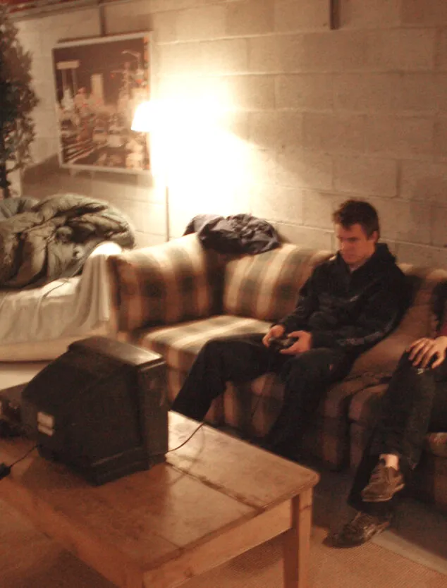 a blurry, warm toned image of two individuals seen sititng on a plaid couch and watching a small television atop a coffee table.